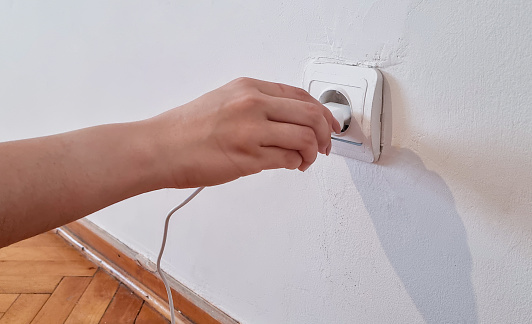 Hand turns on, turns off charger in electrical outlet
