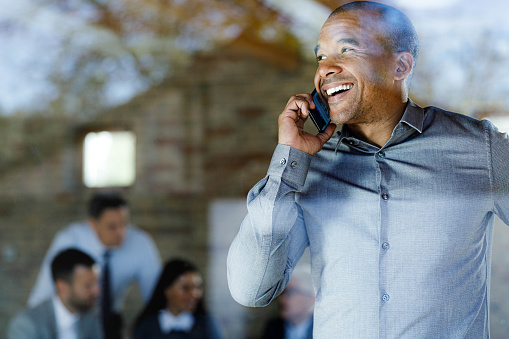 Happy African American entrepreneur communicating with someone over mobile phone in the office. The view is through glass.