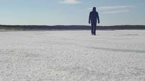 Man Walks in Ice on Remote Frozen Sea Beach on Sunny Winter Day