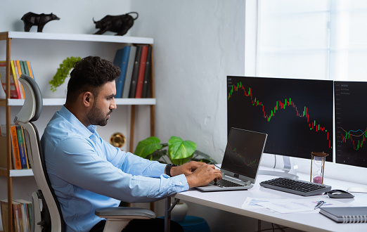 Indian trader or stock Market broker analyzing candle stick graphs on laptop at office - concept of Investment opportunities, Trading strategies and Price movements.