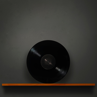 Blank LP Record on a wooden shelf against dark concrete wall with copy space.