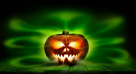 A spooky halloween pumpkin, Jack O Lantern, with an evil spinning green aura glow against a dark background.