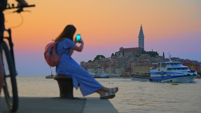 SLO MO Woman Capturing Stunning Old Town of Rovinj from Harbor at Sunset