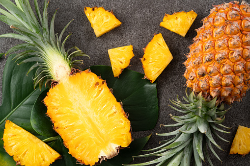 Top view of fresh cut pineapple with tropical leaves on dark gray table background.