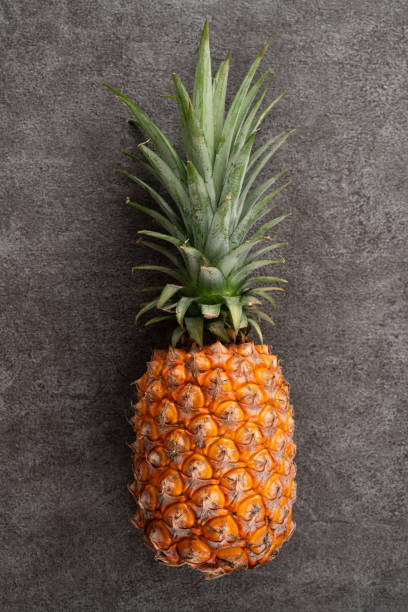 istock Fresh cut pineapple with tropical leaves on dark gray table background. 1571277752