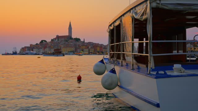 SLO MO Passenger Boat Floating on Sea with Old Town of Rovinj in Background at Sunset