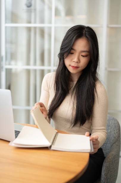 istock A beautiful Asian female college student focuses on reading a book while studying online 1571303048