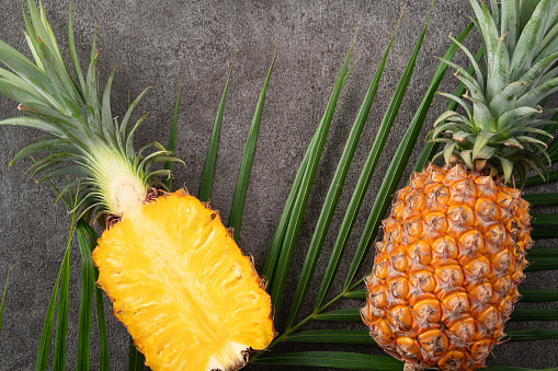Top view of fresh cut pineapple with tropical leaves on gray table background.