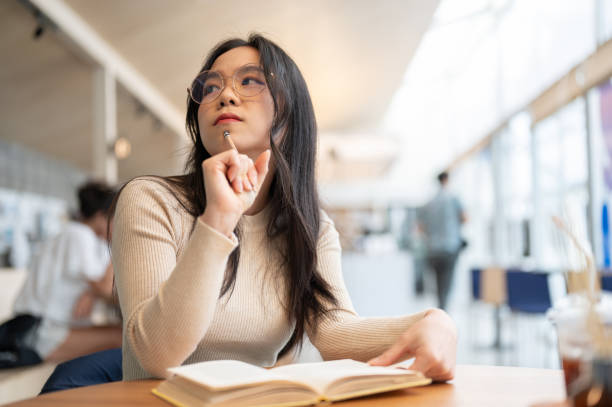 istock A smart and thoughtful Asian female student is planning her project while reading at a library. 1571305738