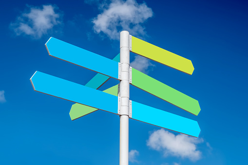Multiple blank coloured signs on a steel pole, pointing in various directions and set against a blue sky.