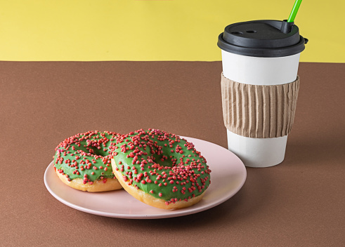 A cup of coffee and two green donuts with red and pink sprinkles on a pink saucer.
