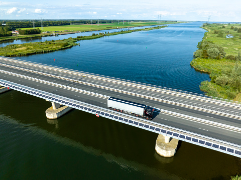 Traffic driving over a bridge over a lake in a nature reserve during a beautiful summer day. The solar panels on the side of the bridge make it a self supporting opening bridge. Overhead drone shot with slight motion blur.