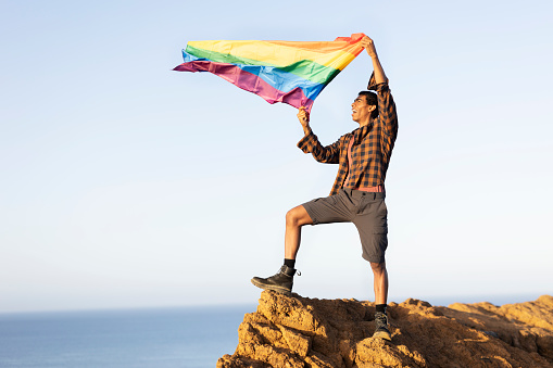 Happy gay man having fun holding rainbow flag symbol of LGBT community.