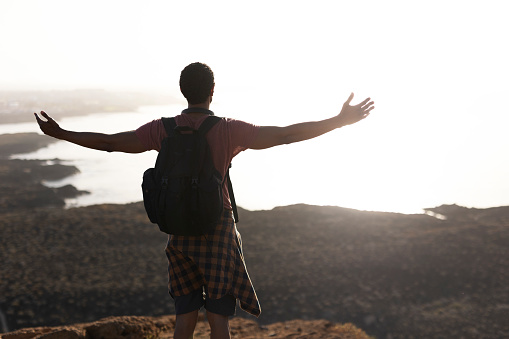 Young man standing on the stone with raised up arms. Tourist man on the top of the mountain.