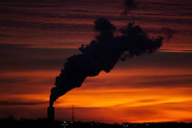 The large dark silhouette of a plume of smoke from a tower against a bright orange sunset.