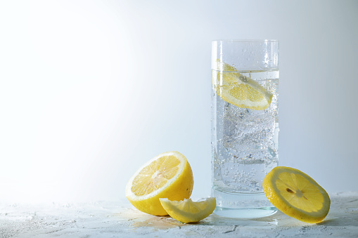 Carbonated soda water with ice cubes and lemon in a drinking glass, refreshing drink against a light gray background, copy space, selected focus, narrow depth of field