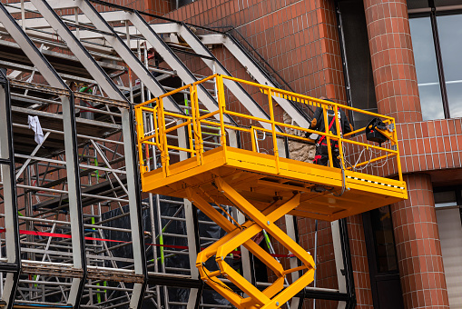 Yellow hydraulic lifting platform with bucket cabin on a telescopic lift near the building structure.