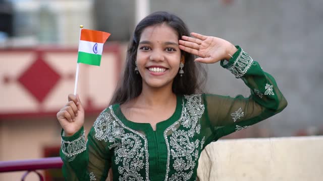 Portrait of Indian woman holding Indian flag and saluting with a smile to the camera.