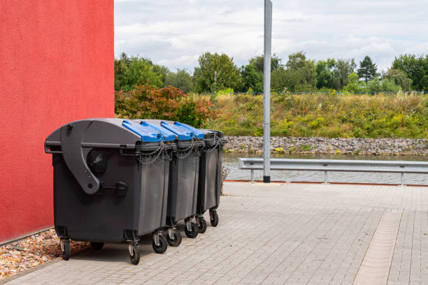 istock Black plastic trash cans closed on a chain stand near a large red building. 1571441717