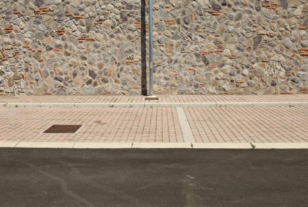 Pole on sidewalk with rustic stone wall on behind and road in front.