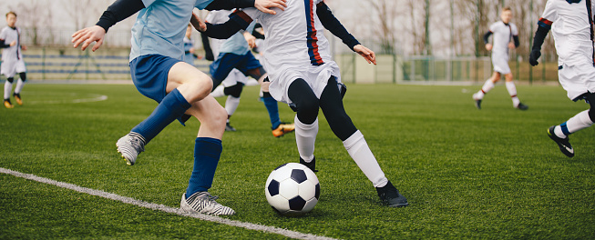 Legs of two young football players on a match. Two soccer players running and kicking a soccer ball.  European football youth player legs in action. Anonymous footballers compete in a football duel