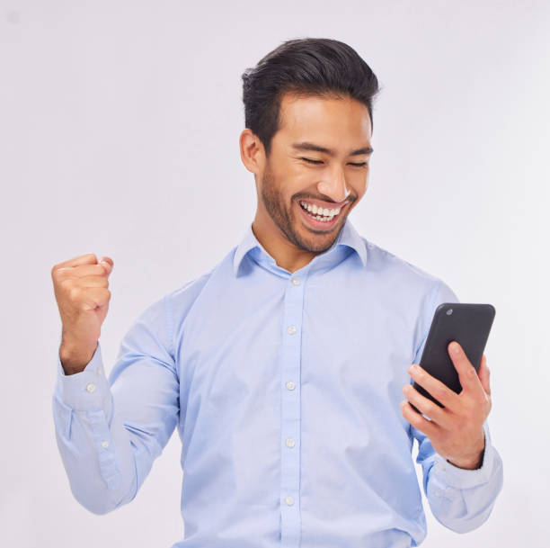 istock Winner, celebration and business man with phone in studio isolated on a white background. Success, cellphone and happy male professional celebrating, bonus or winning prize, competition or lottery. 1571466787