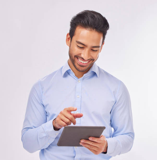 istock Typing, smile and business man with tablet in studio isolated on a white background. Professional, technology and happy male with touch screen for social media, research or internet browsing online. 1571471482