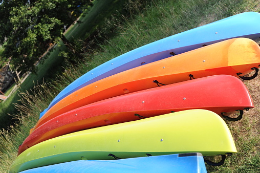 Colorful kayaks stacked in a row on a green meadow on a sunny summer day in Poland