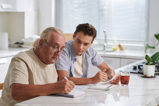 Senior man explaining teenage son how to pay bills