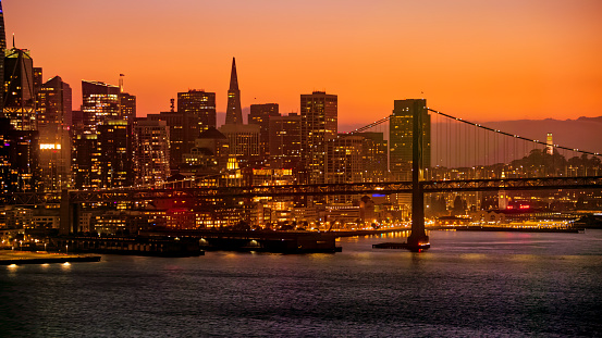 Aerial view of modern skyscraper buildings against bridge in city during dusk, San Francisco, California, USA.