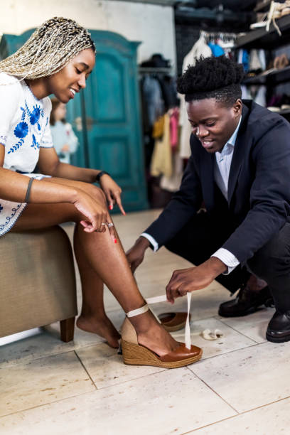 jovem ajuda a namorada a experimentar sapatos novos em loja de roupas - shoe store sales clerk customer - fotografias e filmes do acervo
