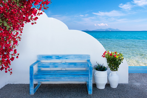 the colors of Greece with a bench on a terrace in front of a wall and a view to the beautiful mediterranean sea