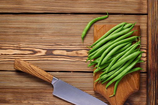 Wooden cutting board with pods of raw asparagus beans and a knife on a wooden background with copy space. Top view.
