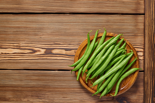 Wooden plate with pods of raw asparagus beans on a wooden background with copy space. Top view.