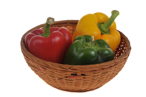 Wicker basket with peppers of different colors close-up on a white background