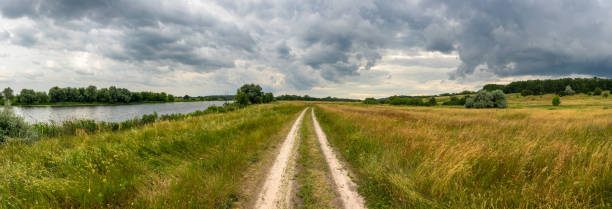 Landscape panorama of a picturesque river valley with a road in a meadow and trees on a cloudy day stock photo