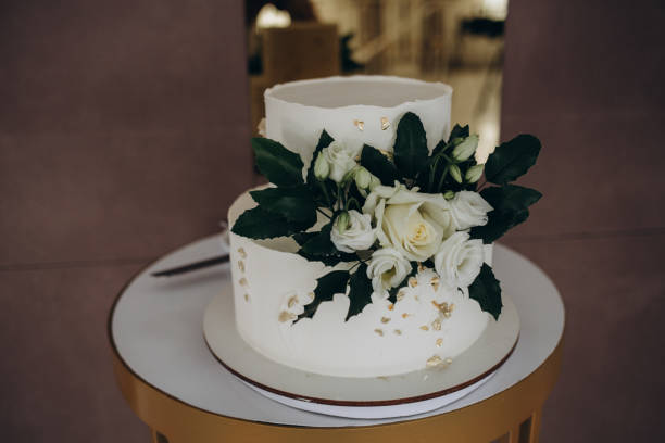 istock Three-tiered white wedding cake decorated with flowers from mastic on a white wooden table. Picture for a menu or a confectionery catalog with copy space. 1571530230