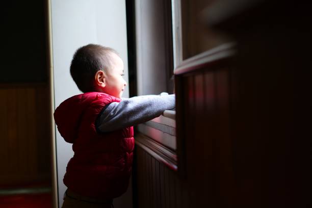 istock Boy looking out window in black and white light 1571540509