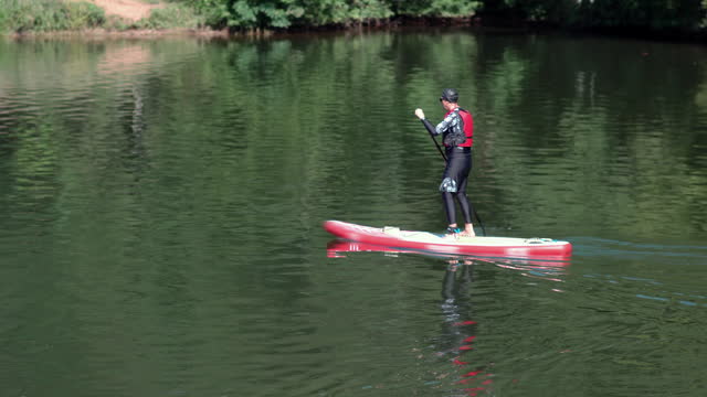 Fit man is training SUP (standup) paddle board in large lake, river on a sunny morning with forest reflection on the water surface. Stand up paddle boarding concept