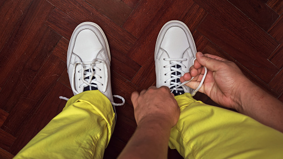 In this top view photo, a stylish man sits indoors, preparing for the day ahead. With meticulous attention to detail, he ties the laces of his fashionable boots. The close-up shot captures the beauty of the lace being skillfully wrapped around his foot, exuding a sense of trendy elegance. This image showcases the art of personal style and the importance of proper shoe preparation. Whether for a business meeting or a casual outing, he ensures his footwear reflects his impeccable taste and comfort. Experience the satisfaction of a well-dressed lifestyle with attention to every detail, from gloss to trendiness