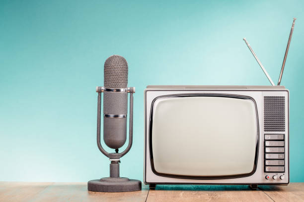 istock Vintage old television and microphone on wooden table front gradient mint blue wall background. Retro style filtered photo 1571568895