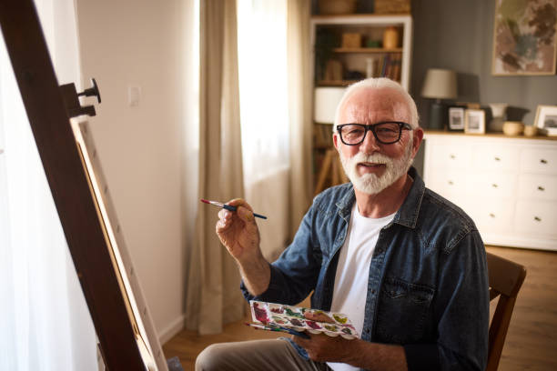 istock Elderly man painting on a canvas at home 1571569440