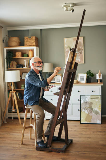 istock Elderly man painting on a canvas at home 1571570537