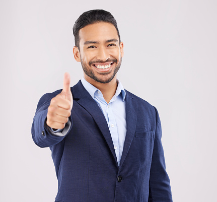 Happy businessman, portrait and thumbs up for success, approval or winning against a grey studio background. Asian man smile with like emoji, yes sign or good job for business agreement and thank you