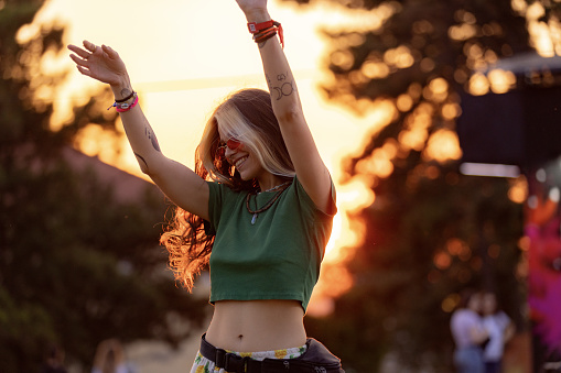 Carefree woman having fun while dancing on an outdoor music festival at sunset.