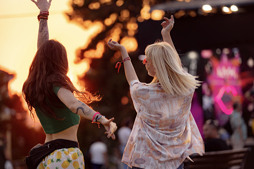 Carefree women having fun while dancing on an outdoor music festival at sunset.