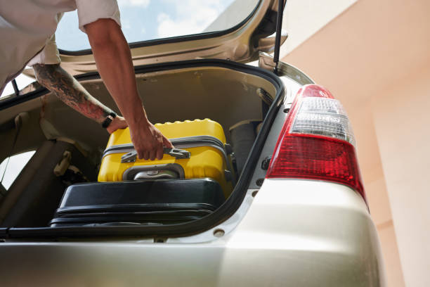 Closeup image of driver taking suitcase out of car truck after arriving to hotel