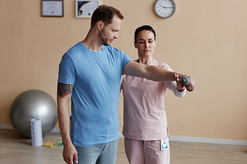Patient exercising with dumbbells together with therapist during rehabilitation