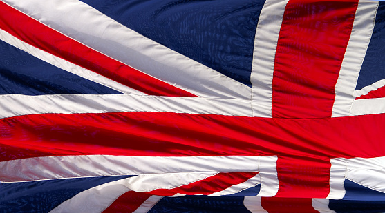 The flag of the United Kingdom of Great Britain and Northern Ireland, known as Union Flag or Union Jack, hanging down loosely at full-mast on a white pole against blue sky.