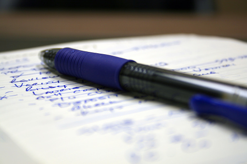 Bright blue pen laying on a long, partially completed, to-do list.  Taken with shallow depth of field.